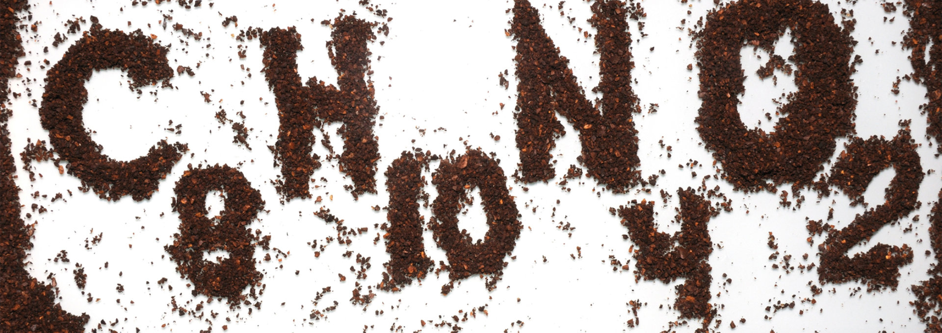 Auf einer weißen Fläche sind die chemischen Symbole und Zahlen "C8H10N4O2" mit braunem Pulver, wahrscheinlich Kaffeepulver, dargestellt. Die Buchstaben und Zahlen sind deutlich sichtbar und kontrastieren stark mit dem weißen Hintergrund, wodurch die chemische Formel, die für Koffein steht, hervorgehoben wird. Die Szene ist umgeben von einer dunkelbraunen Textur, die an Kaffee oder Erde erinnert.