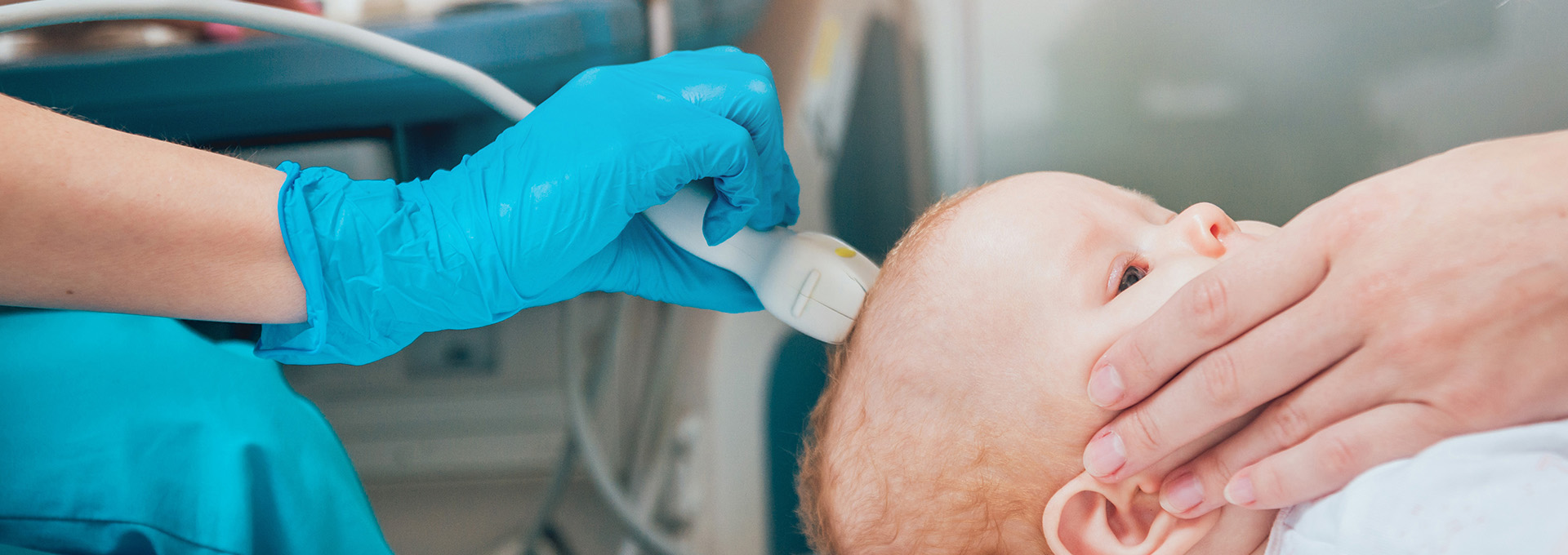 Kleines Baby liegt mit dem Bauch nach unten und eine Arzt-Hand hält ein medizinisches Gerät an den Nacken