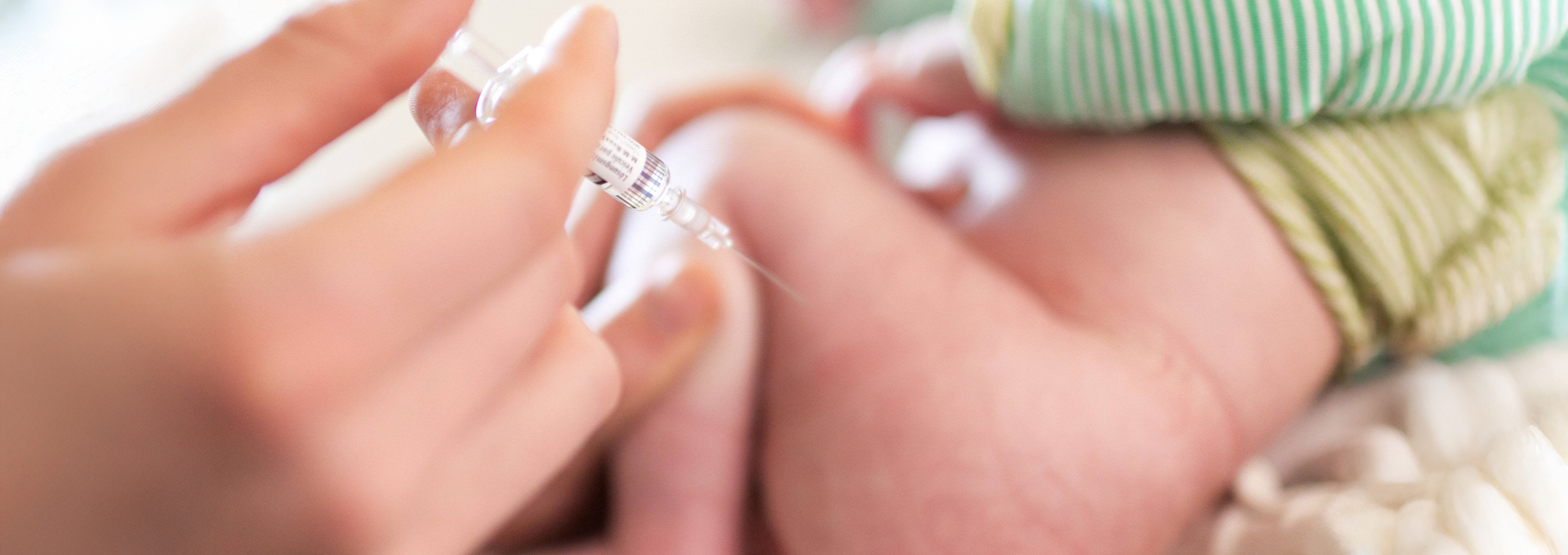 Eine Hand verabreicht einem Baby eine Impfspritze in den Oberschenkel