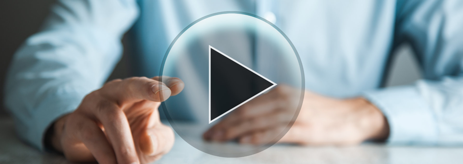 Person sitzt am Tisch und tippt mit zwei Fingern auf ein Handy, davor schwebt ein Play-Button in der Luft