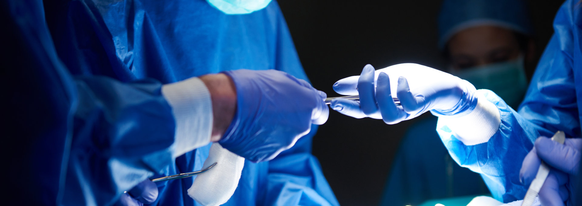 blau gekleidete Ärzte, im Vordergrund reichen sich zwei Ärzte mit blauen OP-Handschuhen ein OP-Werkzeug