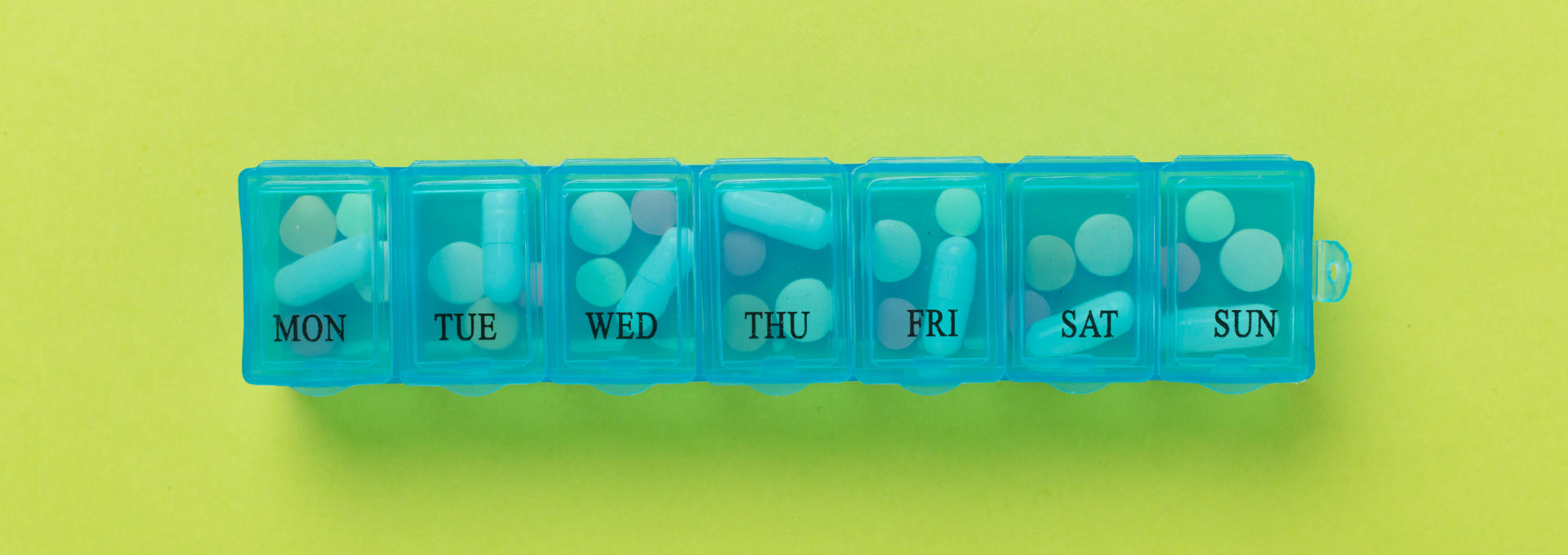 Eine gefüllte Tablettenbox mit Wocheneinteilung auf grünem Hintergrund