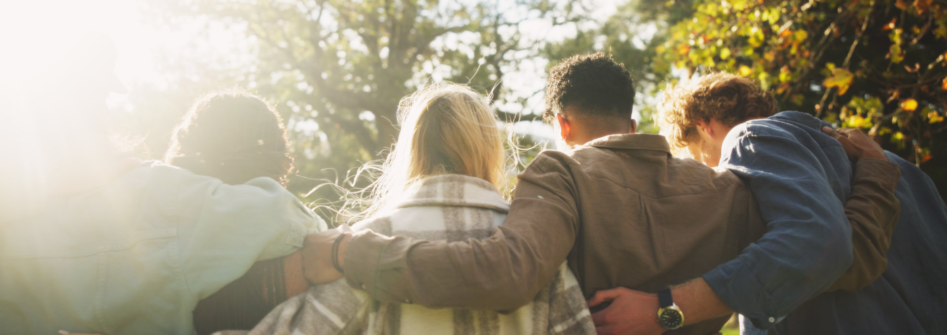 Vier Freunde stehen Arm in Arm draußen im Sonnenlicht