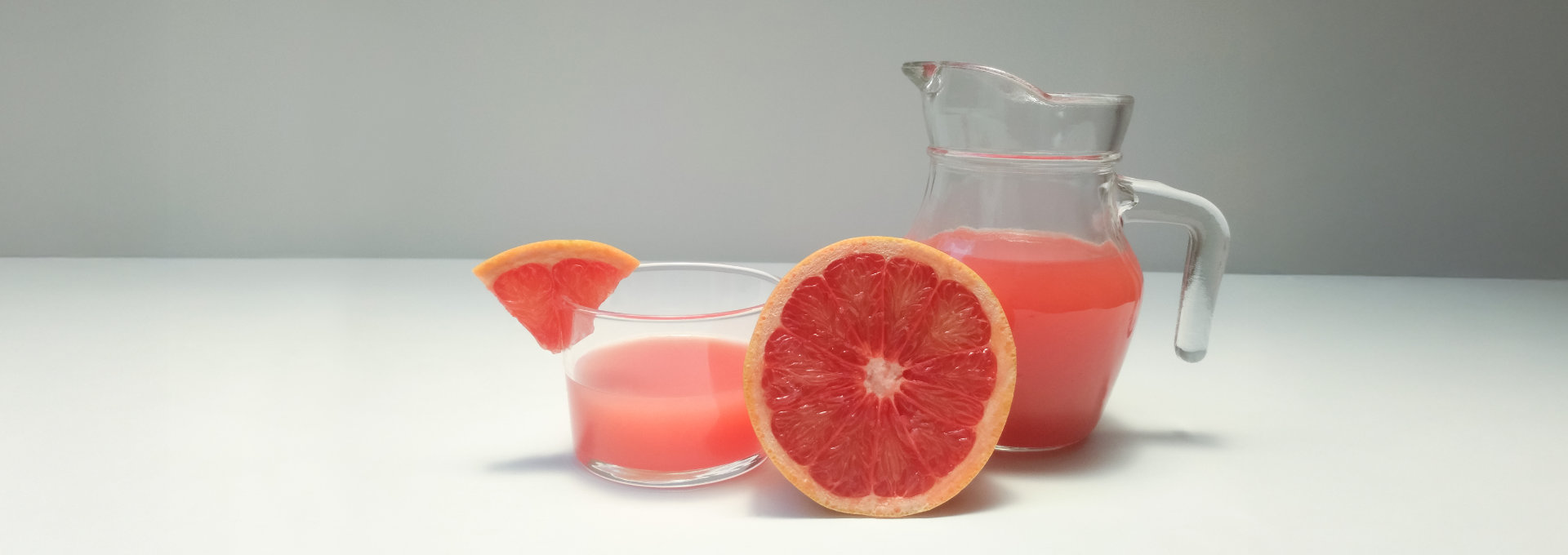 Ein Glas und eine Karaffe mit frischem Grapefruitsaft, daneben eine aufgeschnittene Grapefruit.